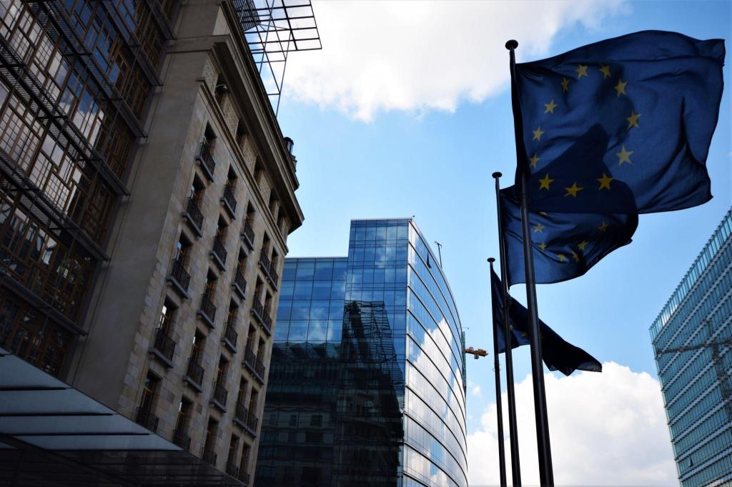 European Union flags flying in front of modern and historic buildings in Brussels under a blue sky.