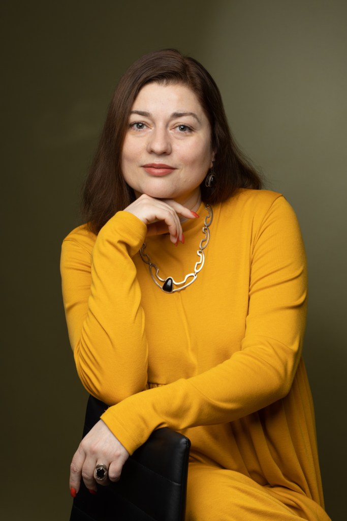 Portrait of Mariya Yasenovska, EEG Coordinator and Advocacy Officer, seated and wearing a yellow dress.